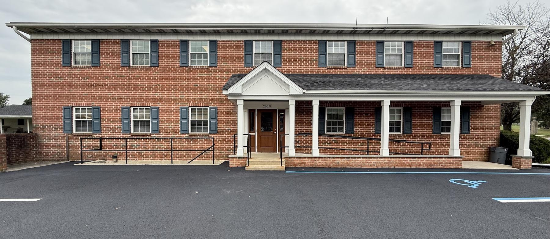The front of the office at 2610 Walbert Avenue: a two-story brick building with dark shutters, a white-columned porch across the entrance, and a freshly paved lot.